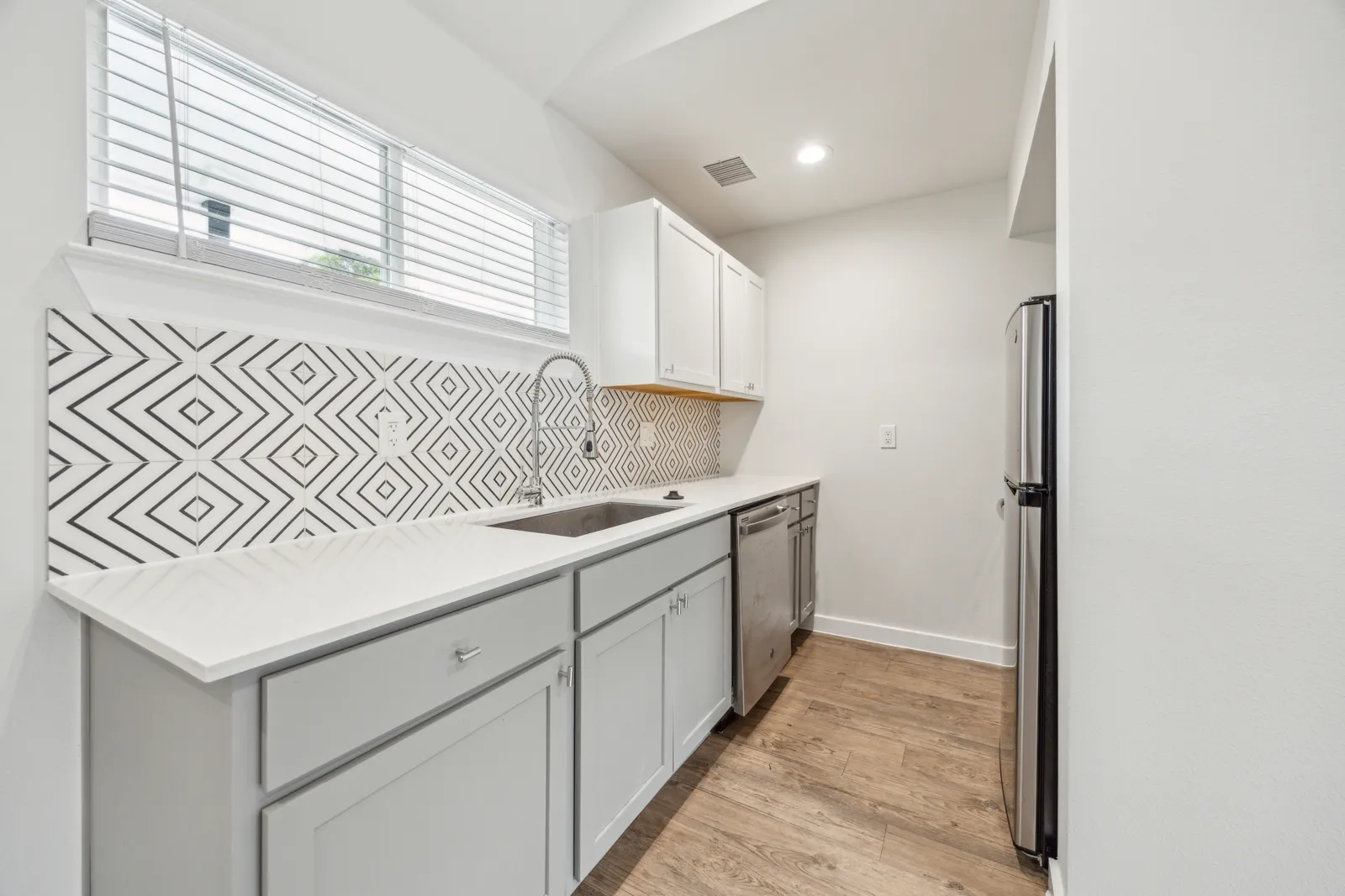 Renovated kitchen with white quartz counters, geometric tile backsplash, and stainless steel appliances
