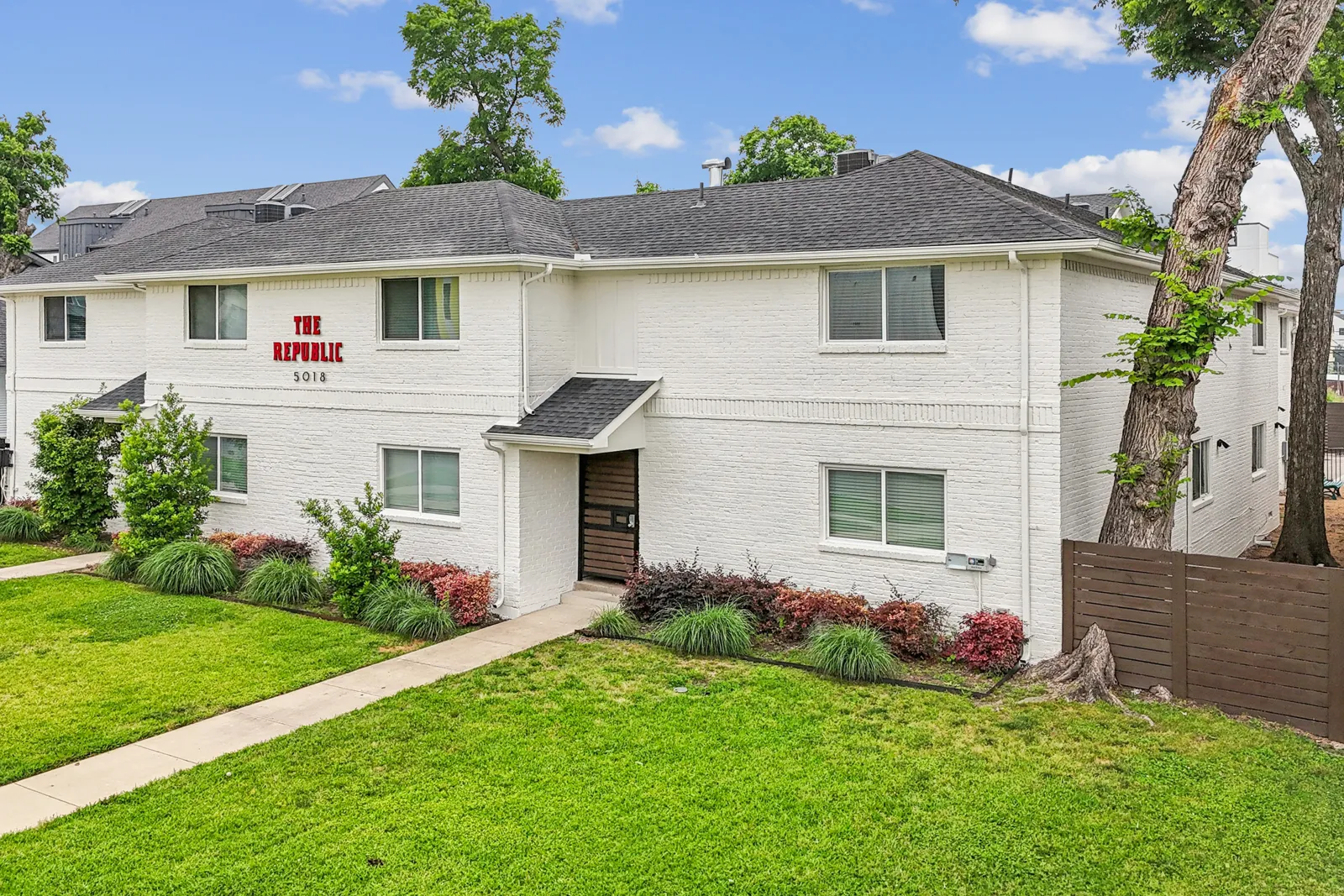 The Republic apartments at 5018 San Jacinto St, Dallas — white brick two-story building with red signage, landscaped lawn, and gated entries
